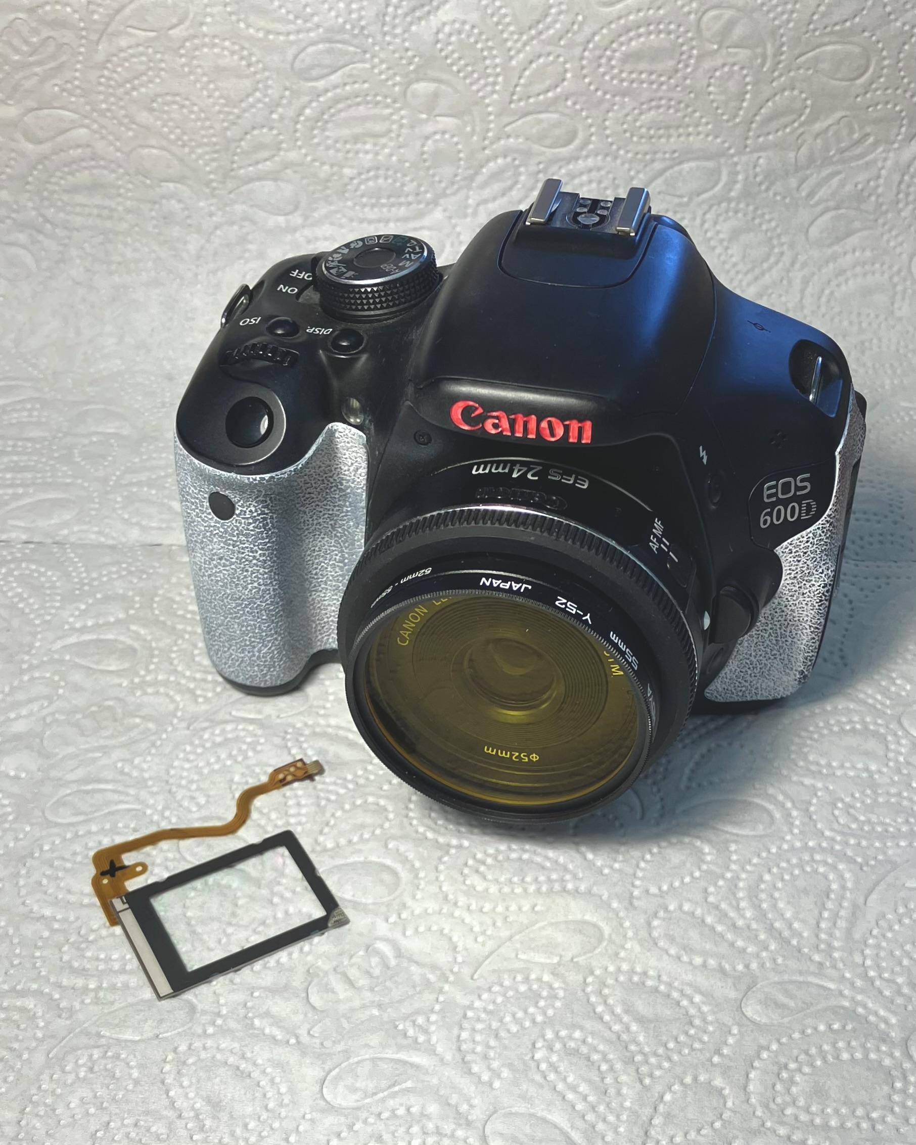 A photo of a canon eos 600d with a yellow coloured filter on its lens. A glass plane with a flatflex cable lays next to the camera.